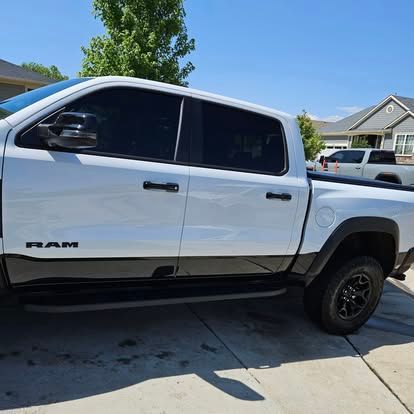 A white RAM truck with black accents and tinted windows is parked on a driveway in front of suburban houses.
