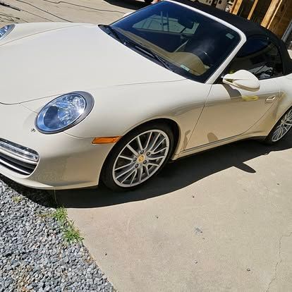 A cream-colored Porsche convertible parked on a concrete driveway next to a gravel patch.