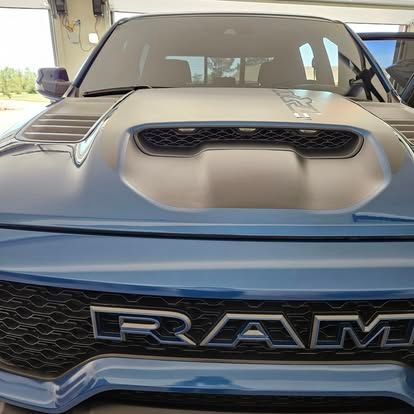 Front view of a blue RAM truck with a large hood scoop and a prominent RAM logo on the black mesh grille.