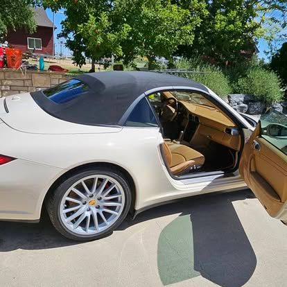 A beige Porsche convertible with a black soft top and tan interior, parked outdoors with the driver-side door open.