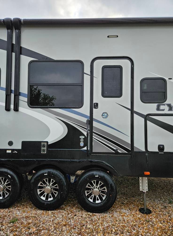 Side view of a parked recreational vehicle featuring a door, two dark windows, graphic decals, and three black wheels.