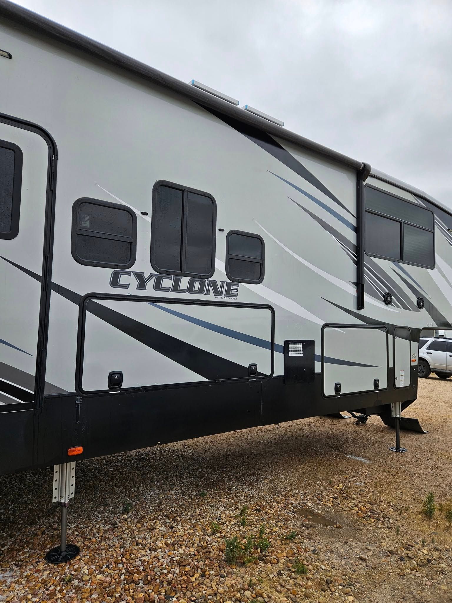 A side view of a grey and black Cyclone toy hauler RV parked on a gravel lot under a cloudy sky.