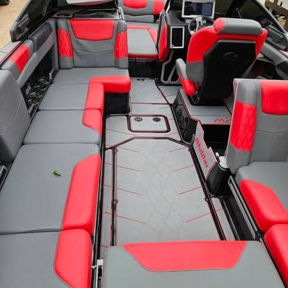 A boat interior with gray and vibrant red upholstered seating, a central walkway, and a captain’s chair at the console.