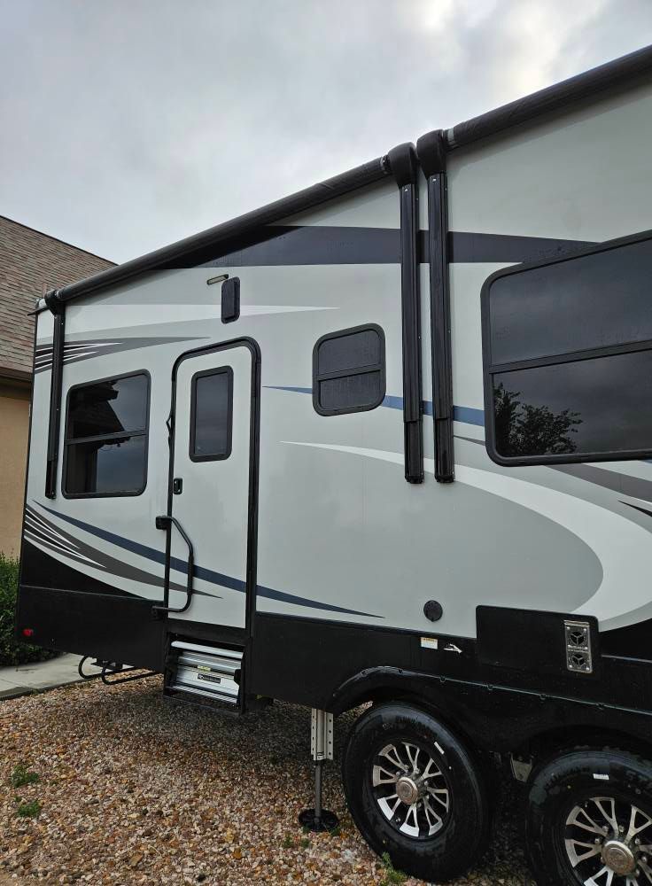 Side view of a modern recreational vehicle parked on gravel with its entry door and awning arms visible.