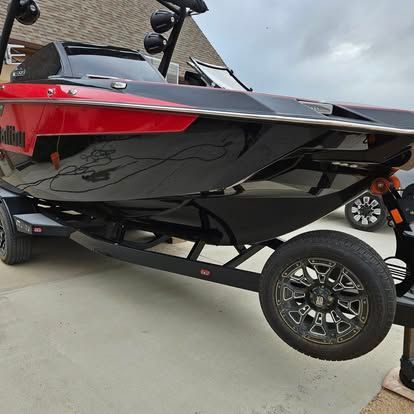 A sleek black and red wakeboard boat on a dark trailer parked on a concrete driveway.