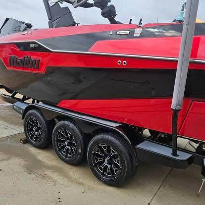 A red and black Malibu boat on a tri-axle trailer, parked on a concrete surface.