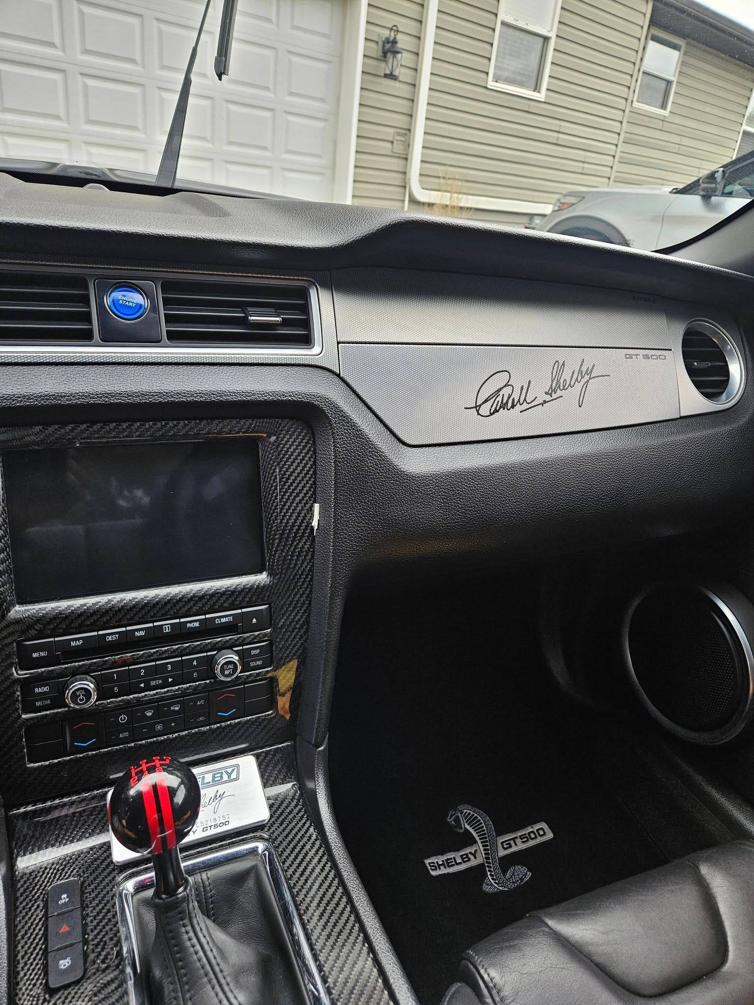 The interior of a Mustang featuring a carbon-fiber dashboard, a signed passenger-side panel, and cobra-branded floor mats.
