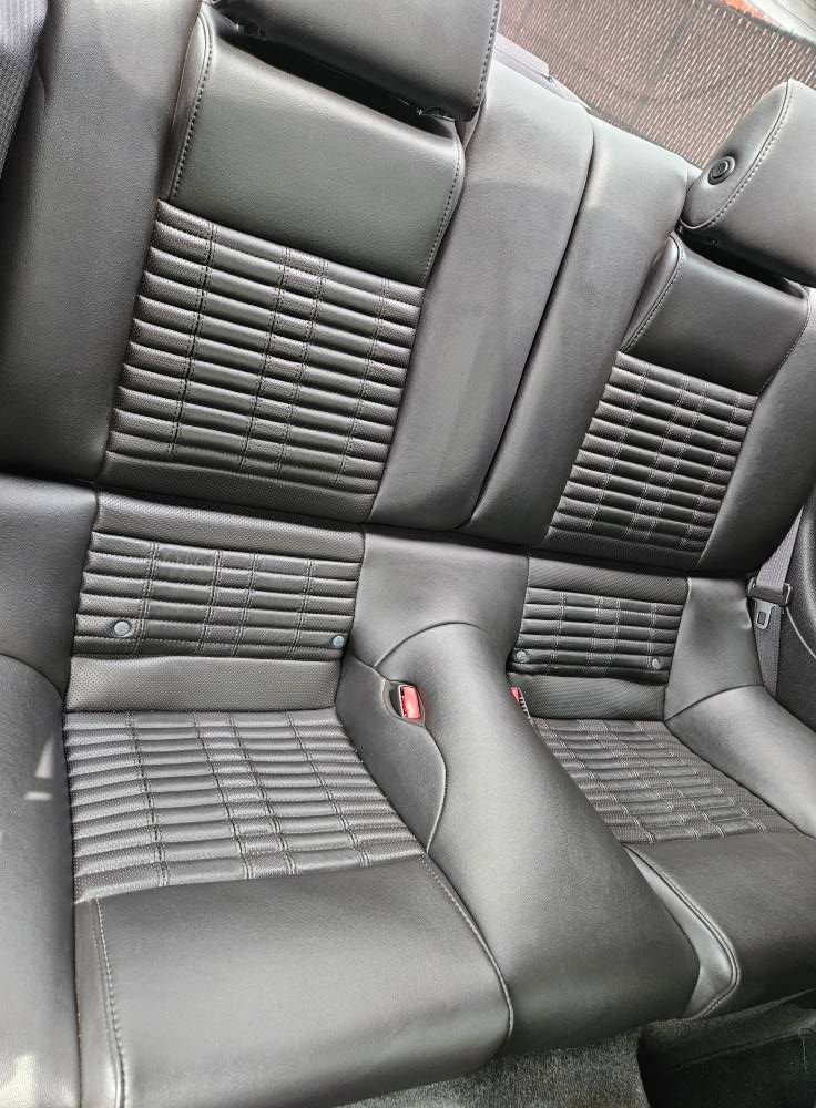 Black leather car backseat with a textured, quilted center pattern and integrated headrests.