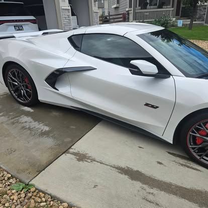 A white Chevrolet Corvette C8 sports car with red brake calipers parked on a residential driveway.