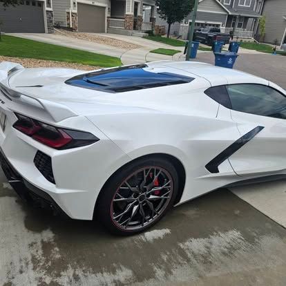A white Chevrolet Corvette C8 parked on a residential driveway in a suburban neighborhood.