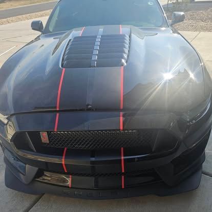 A front-view, high-angle shot of a black Ford Mustang with prominent red racing stripes and a ventilated hood.