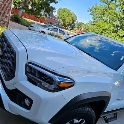 A close-up of a white Toyota Tacoma pickup truck parked on a sunny day, focusing on the front grille and headlights.