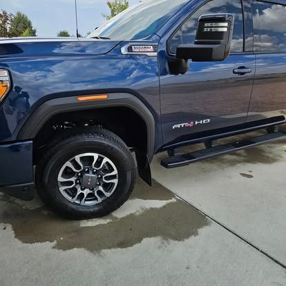 A dark blue GMC Sierra HD pickup truck parked on concrete, showing the front driver-side wheel, cab, and side mirror.
