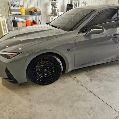 A gray Lexus sedan with black wheels parked inside a brightly lit garage.