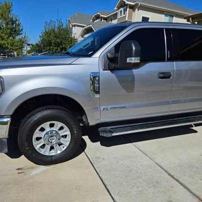 A silver Ford Super Duty pickup truck is parked on a concrete driveway in front of a house.