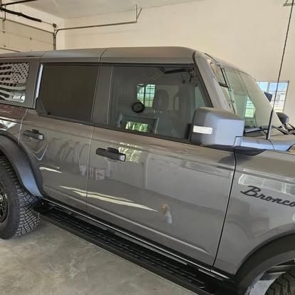 A gray Ford Bronco parked in a garage, featuring black trim, window shades, and 