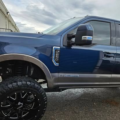 A blue Ford Super Duty truck with large, custom wheels and silver trim parked on an asphalt surface.