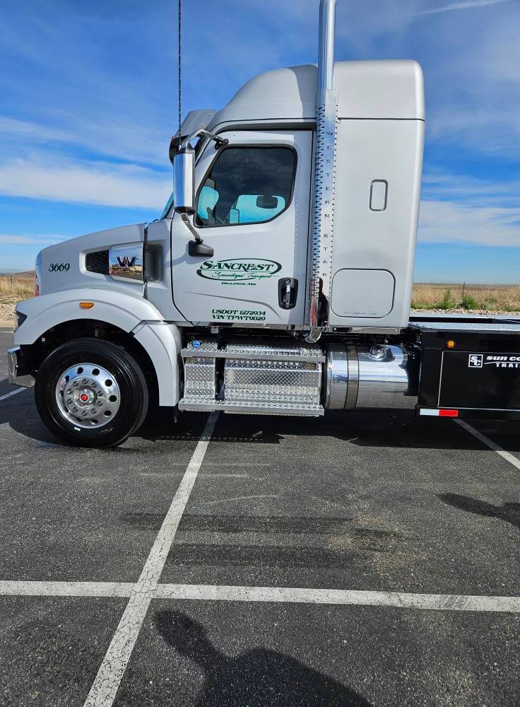 A silver semi-truck parked in an outdoor lot under a clear blue sky.