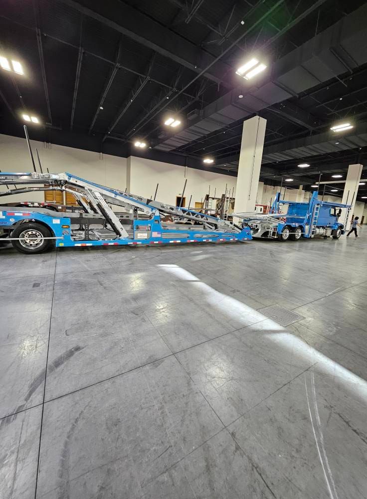 Two blue car-hauler trailers parked inside a large, brightly lit warehouse with a concrete floor.