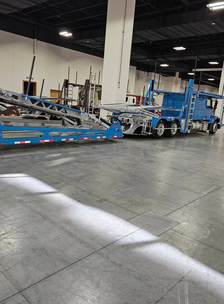 A blue car hauler truck parked inside a large, industrial warehouse with concrete floors.