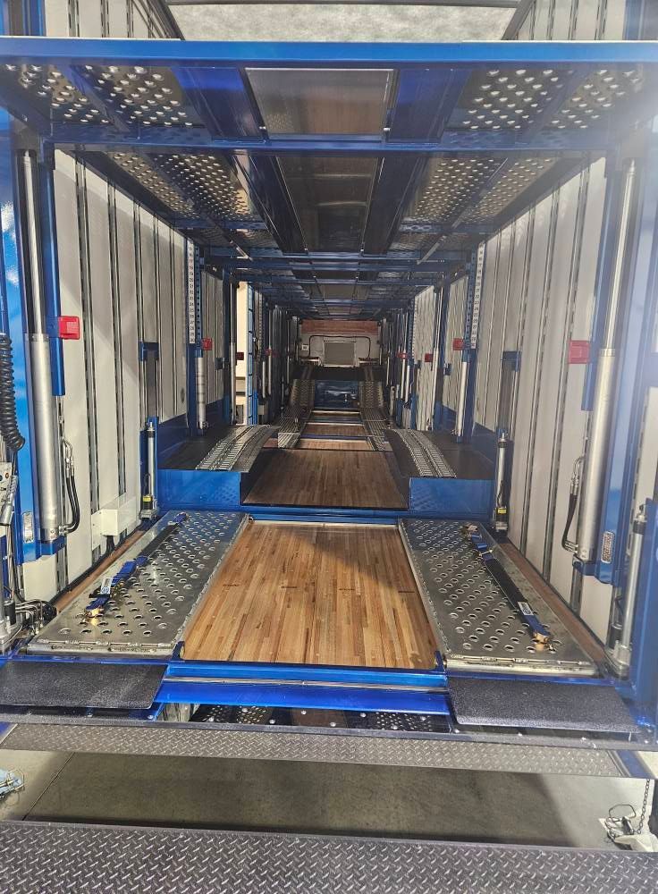 Interior view of an empty blue car hauler trailer with wooden flooring and adjustable metal tracks.