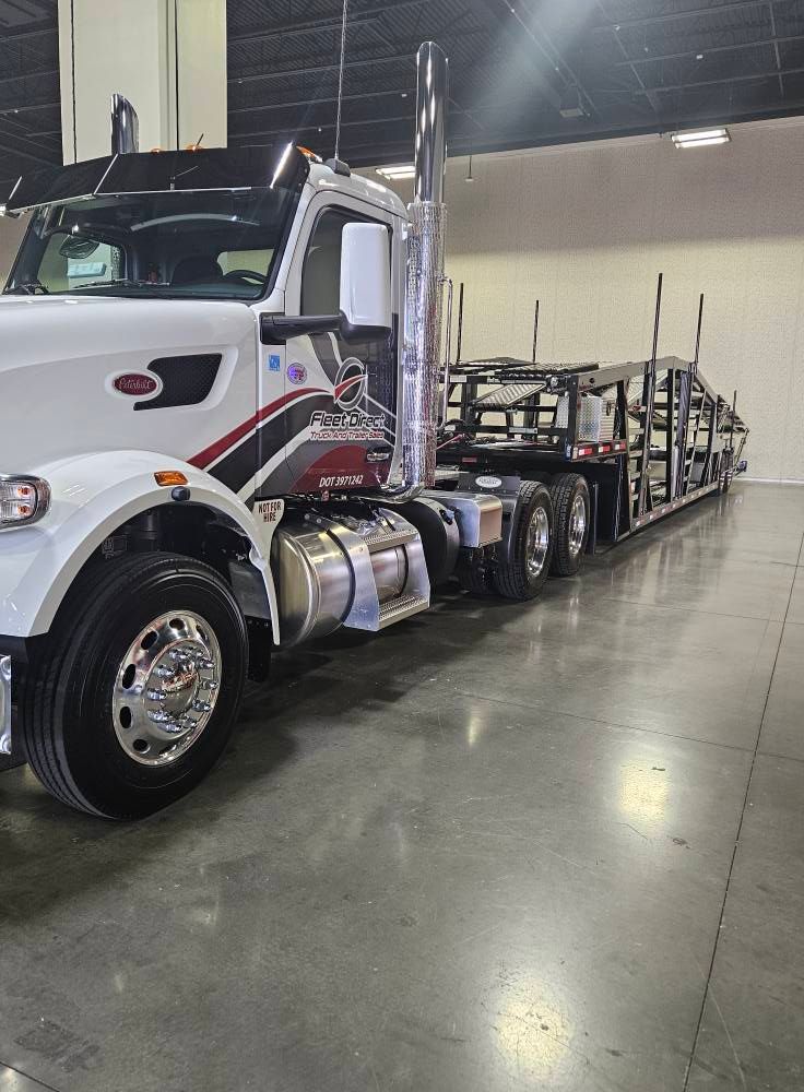 A white Peterbilt semi-truck with a car hauler trailer parked inside a well-lit, industrial facility.