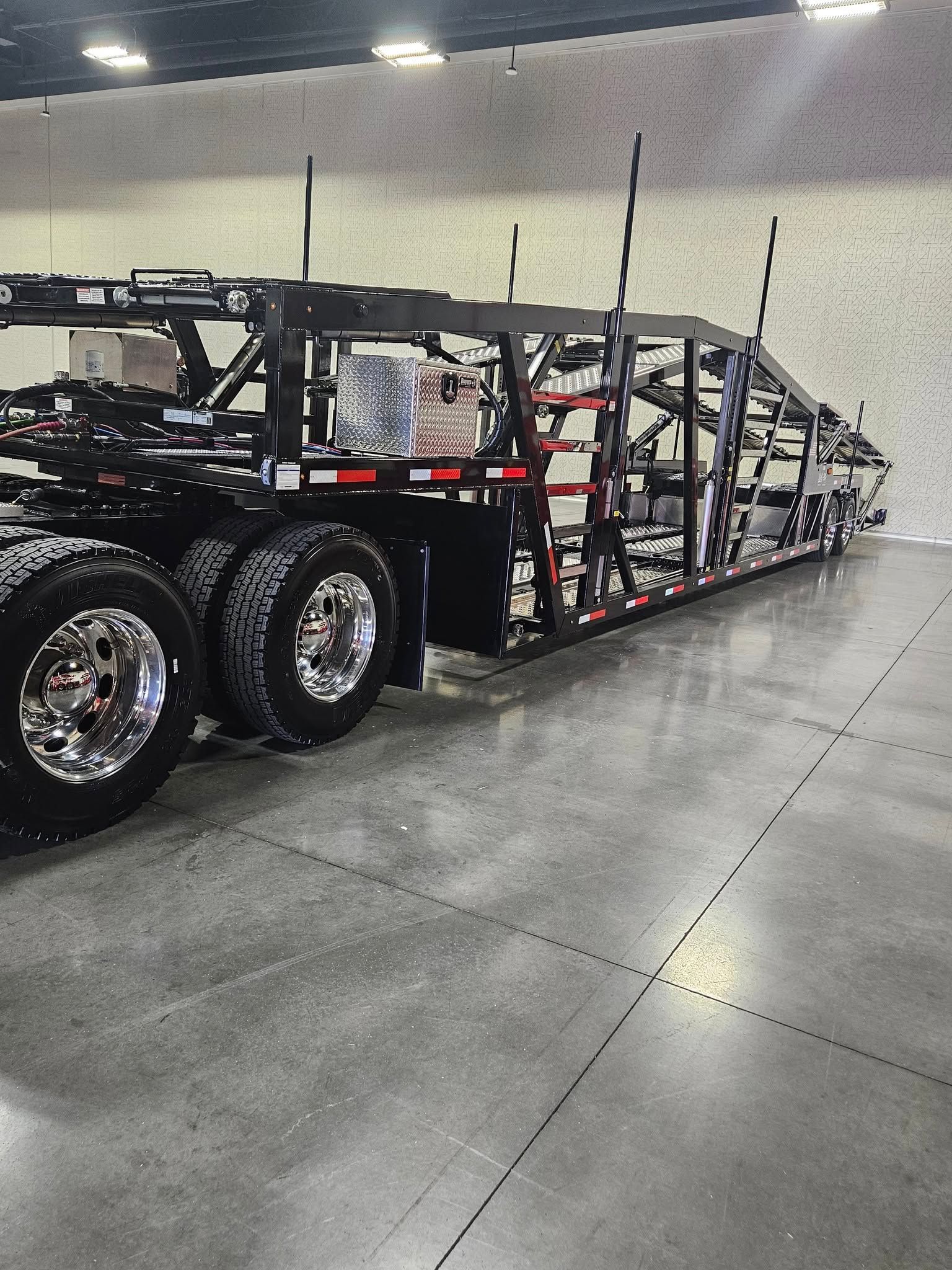 A black car carrier trailer parked on a concrete floor inside a warehouse.