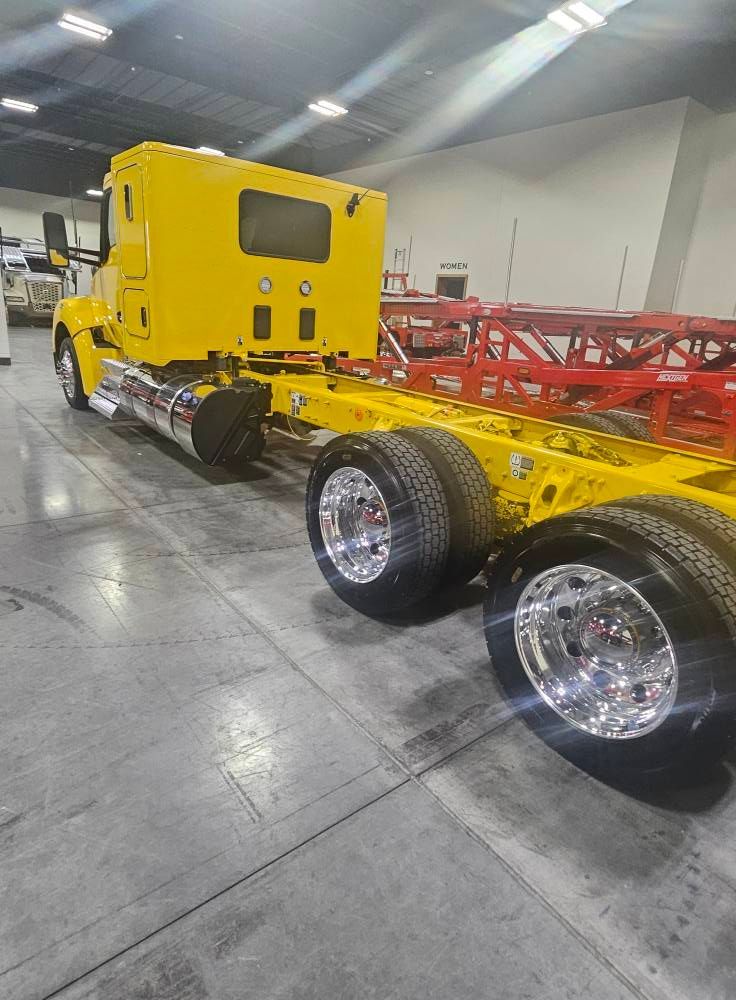 A bright yellow semi-truck cab with a long chassis and shiny chrome wheels parked inside a warehouse.