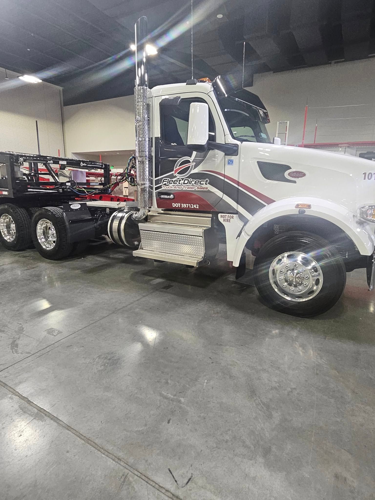 A white Peterbilt semi-truck parked indoors, featuring metallic chrome exhaust stacks and custom side decals.
