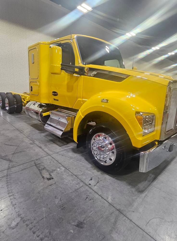 A bright yellow semi-truck parked on a concrete floor in a bright, indoor facility.