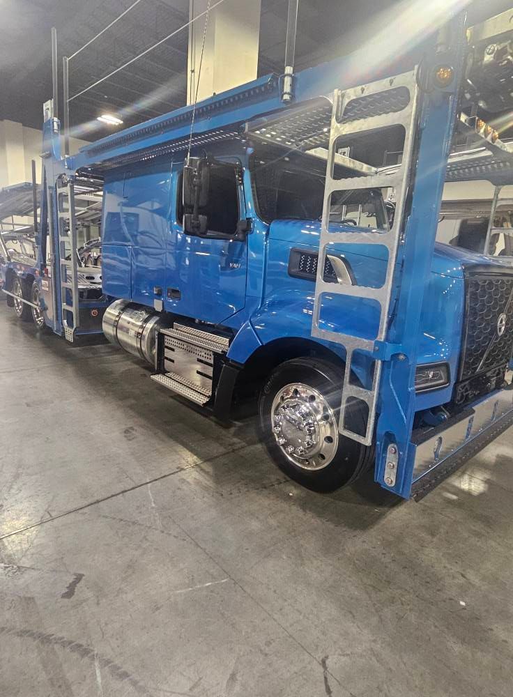 A bright blue car-hauler semi-truck parked inside a large, industrial warehouse space.