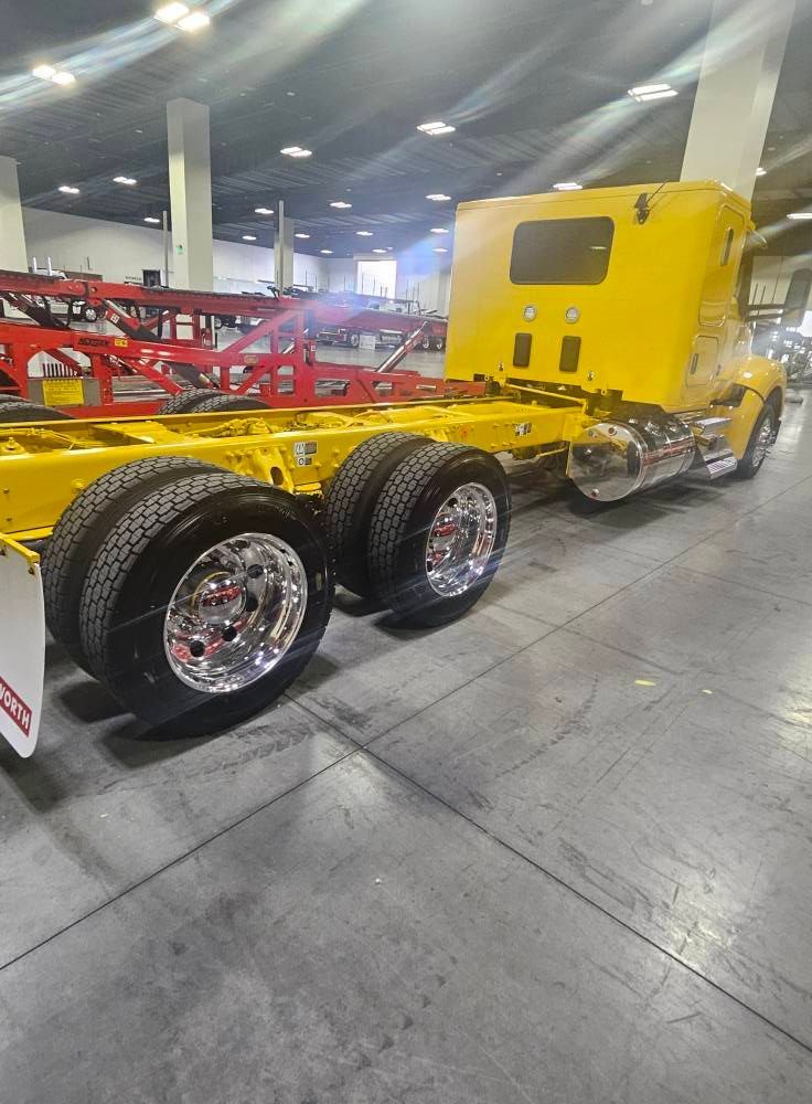 A yellow semi-truck cab with dual rear wheels and a shiny metal fuel tank parked inside a large, industrial warehouse.
