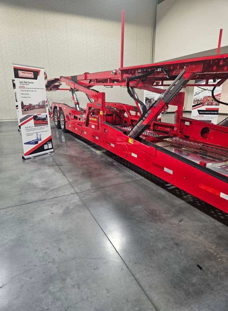 A bright red multi-level car hauler trailer parked on a concrete floor next to an informational banner.