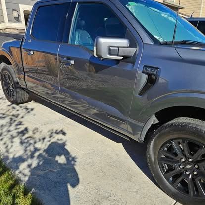 A dark gray Ford F-150 pickup truck parked on a residential driveway on a sunny day.