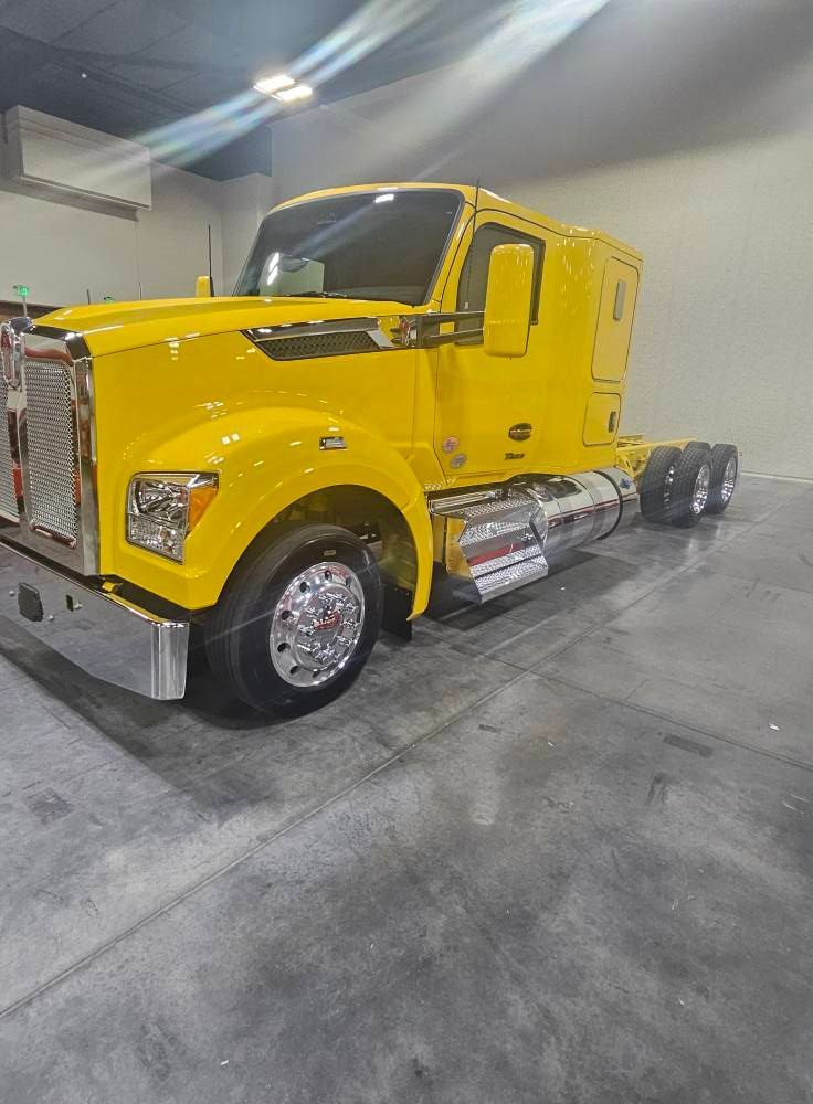 A bright yellow semi-truck parked indoors on a grey concrete floor, featuring chrome details and wheels.
