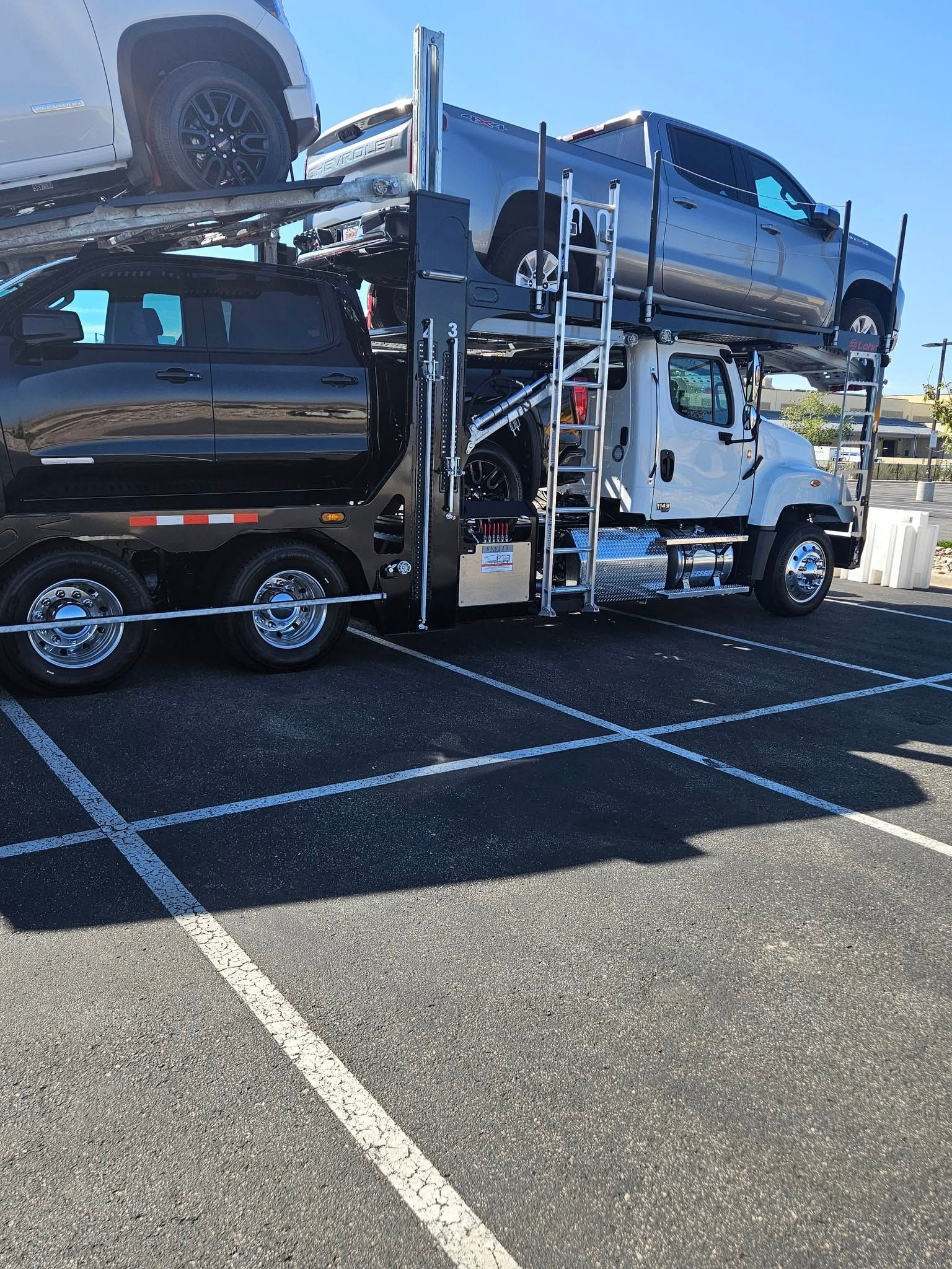 A white commercial car hauler truck parked in a paved lot, carrying multiple SUVs on two levels.