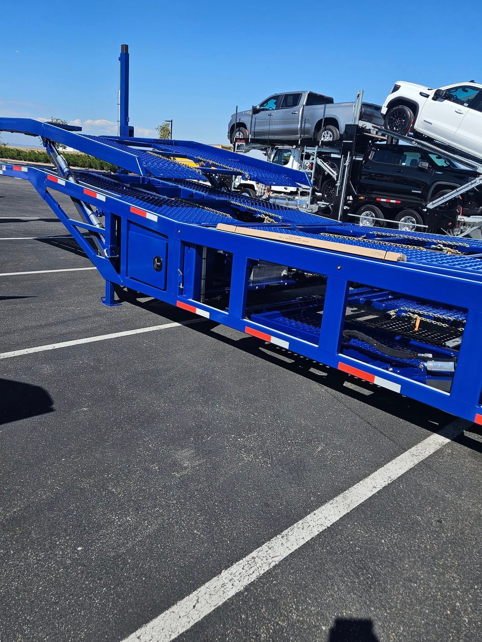 A bright blue multi-car hauler trailer parked in an asphalt lot on a sunny day with vehicles loaded on the upper deck.