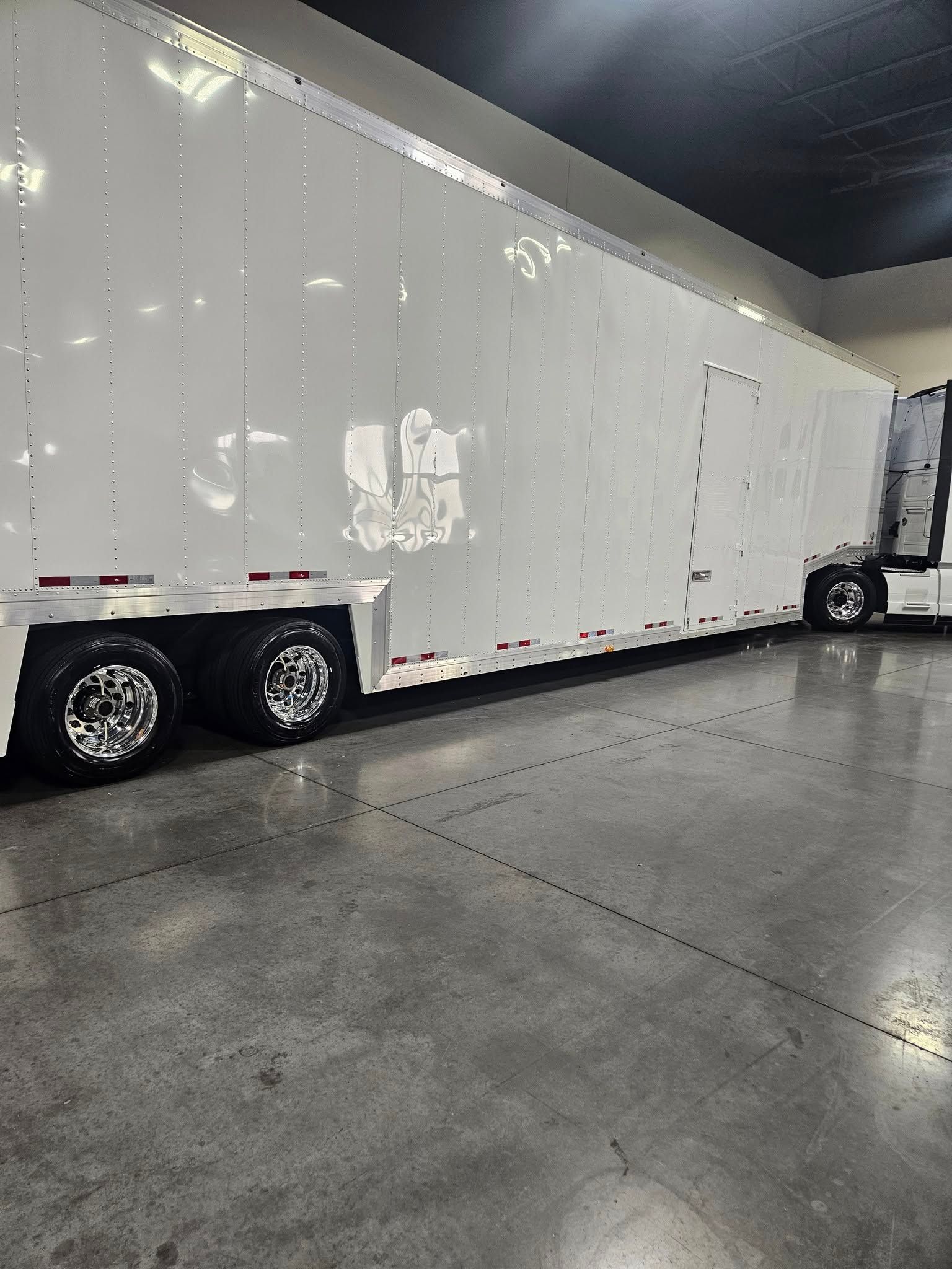 A long, white, enclosed semi-trailer parked on a grey concrete floor in a bright, indoor storage facility.