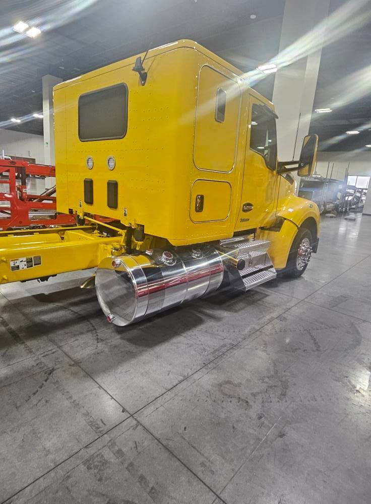 A bright yellow semi-truck cab parked inside a spacious garage with polished floors.