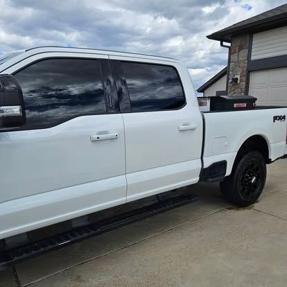 A white Ford F-150 crew cab pickup truck parked on a concrete driveway in front of a house.
