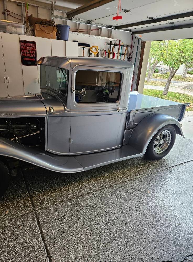 A silver vintage pickup truck parked inside a garage.