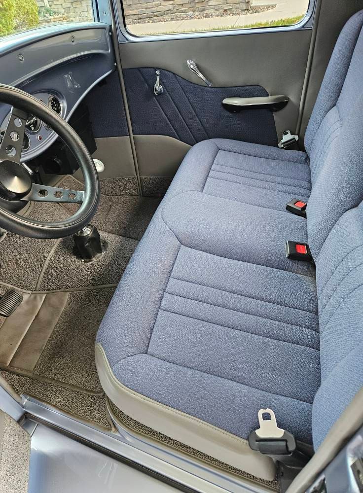 Interior view of a classic car with a blue fabric bench seat, matching door panels, and a dark steering wheel.