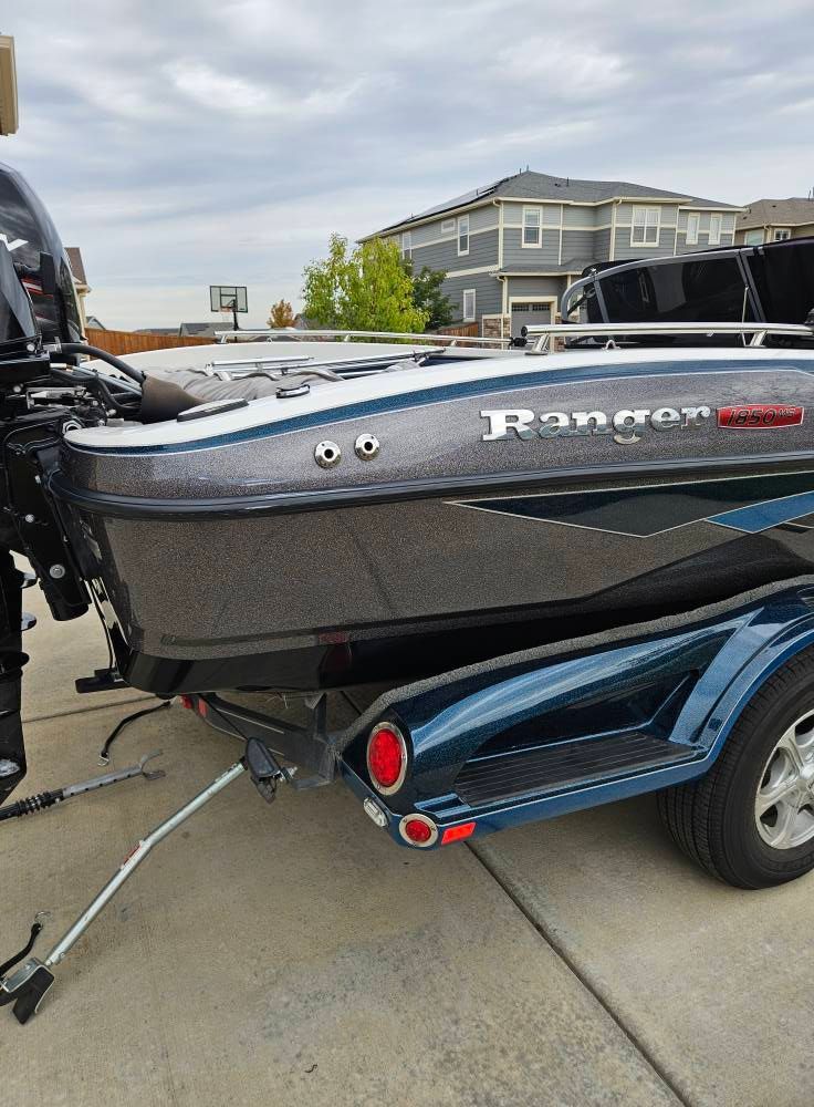 The rear view of a gray Ranger bass boat on a blue trailer, parked on a concrete driveway in front of a suburban house.