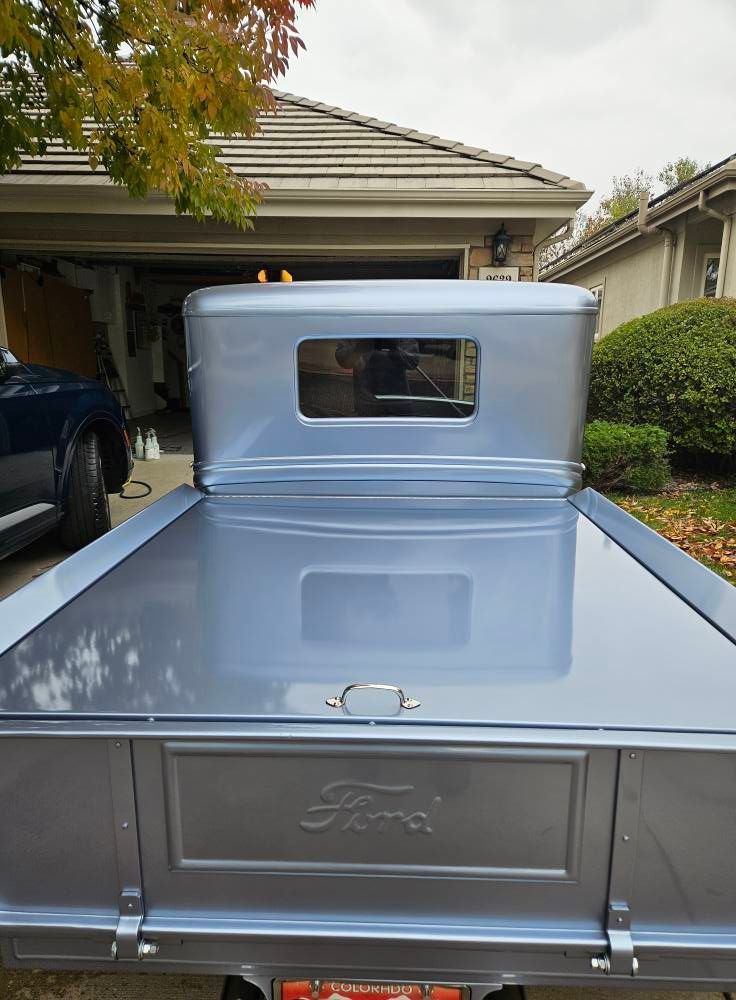 Rear view of a metallic silver vintage Ford pickup truck parked in a residential driveway.