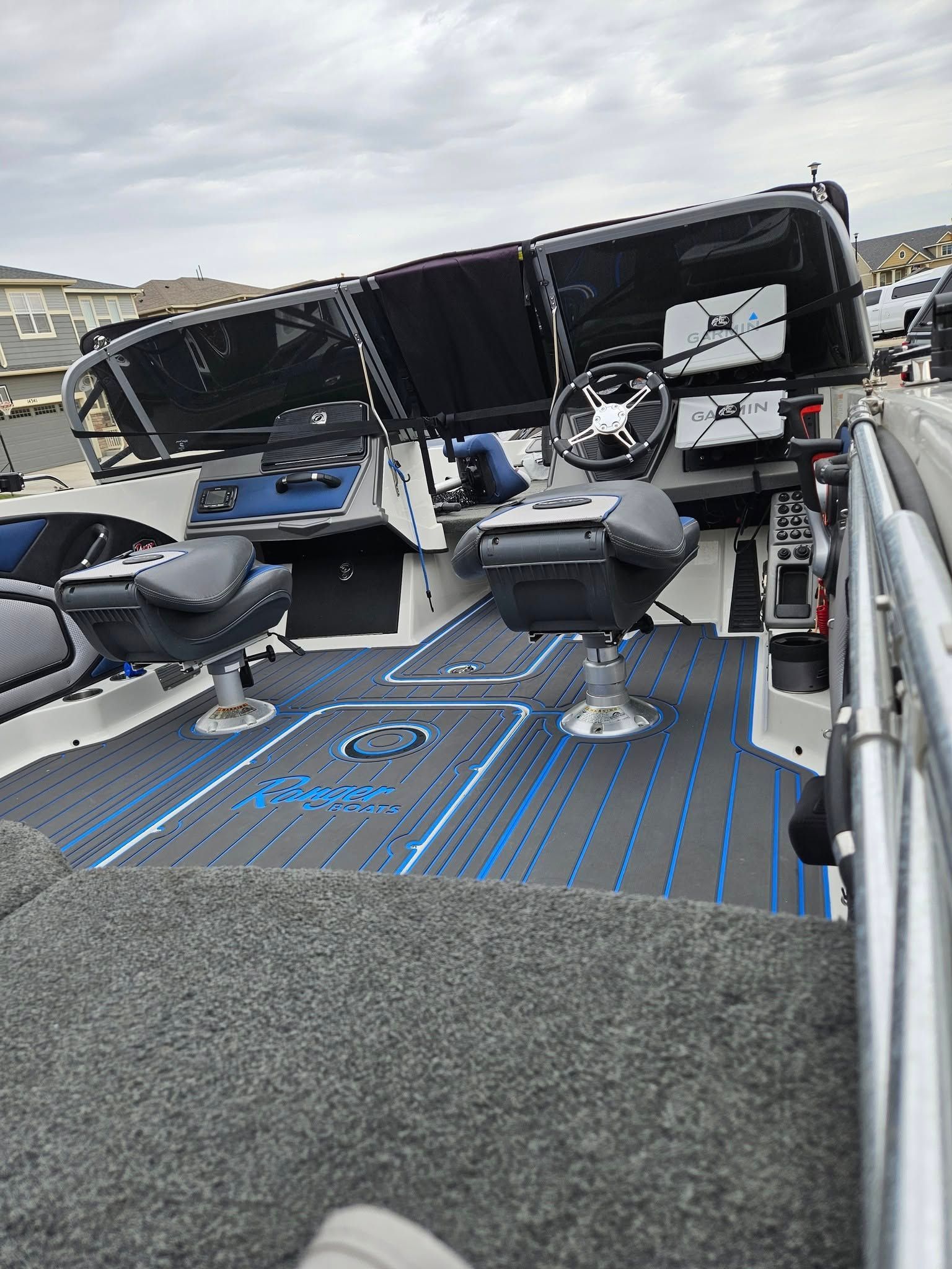 The cockpit of a fishing boat with grey and blue foam decking, two swivel chairs, and a steering console.