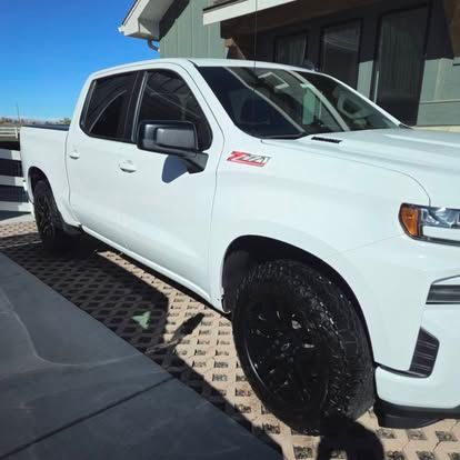 A white Chevrolet Silverado pickup truck with a Z71 badge, parked on a patterned paved driveway near a modern home.