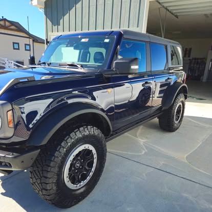A dark blue Ford Bronco parked outdoors next to a building with vertical siding.