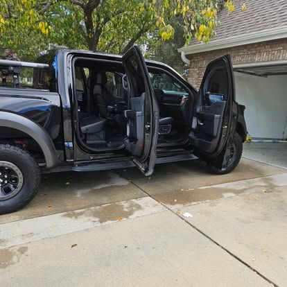 A black pickup truck parked in a driveway with both side doors open, showing the interior.