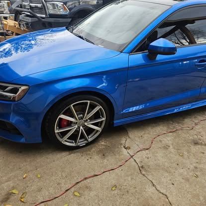 A bright blue Audi sedan parked on a paved lot, showcasing its side profile, multi-spoke wheels, and red brake calipers.