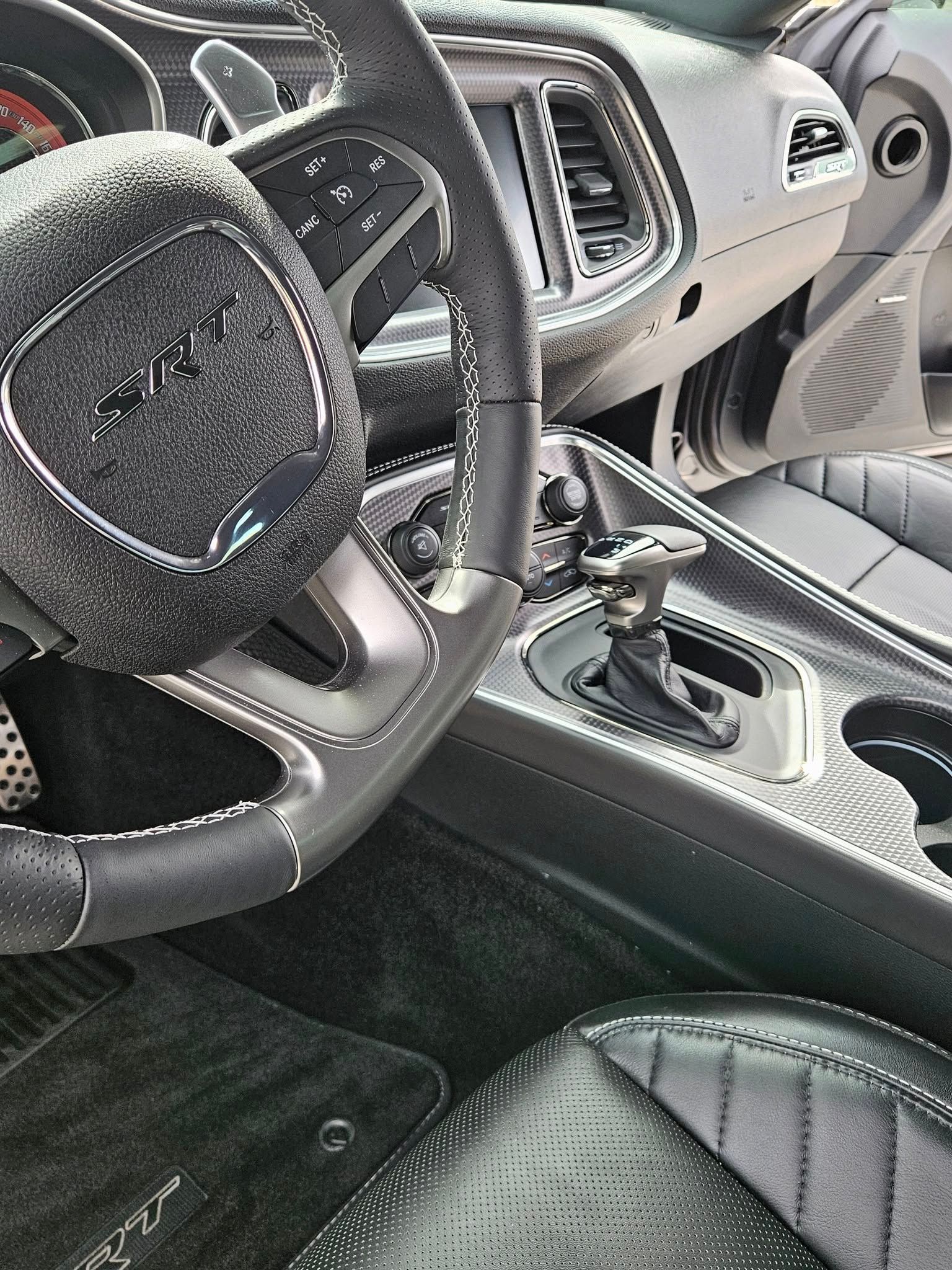 Interior of a Dodge Challenger SRT featuring a black leather steering wheel, carbon fiber trim, and a gear shifter.
